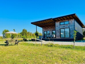Un bâtiment moderne avec une façade en pierre, de grandes fenêtres et un espace extérieur couvert comprenant une table de pique-nique.