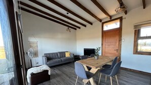 A modern living room with a wooden dining table, grey sofa, and a large window. - Cabañas Lawal Pto Varas (Puerto Varas)