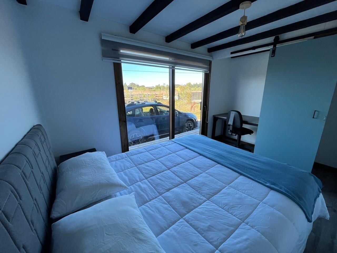 Ein Schlafzimmer mit einem großen Bett, einem Schreibtisch und einem Fenster mit Blick auf parkende Autos.