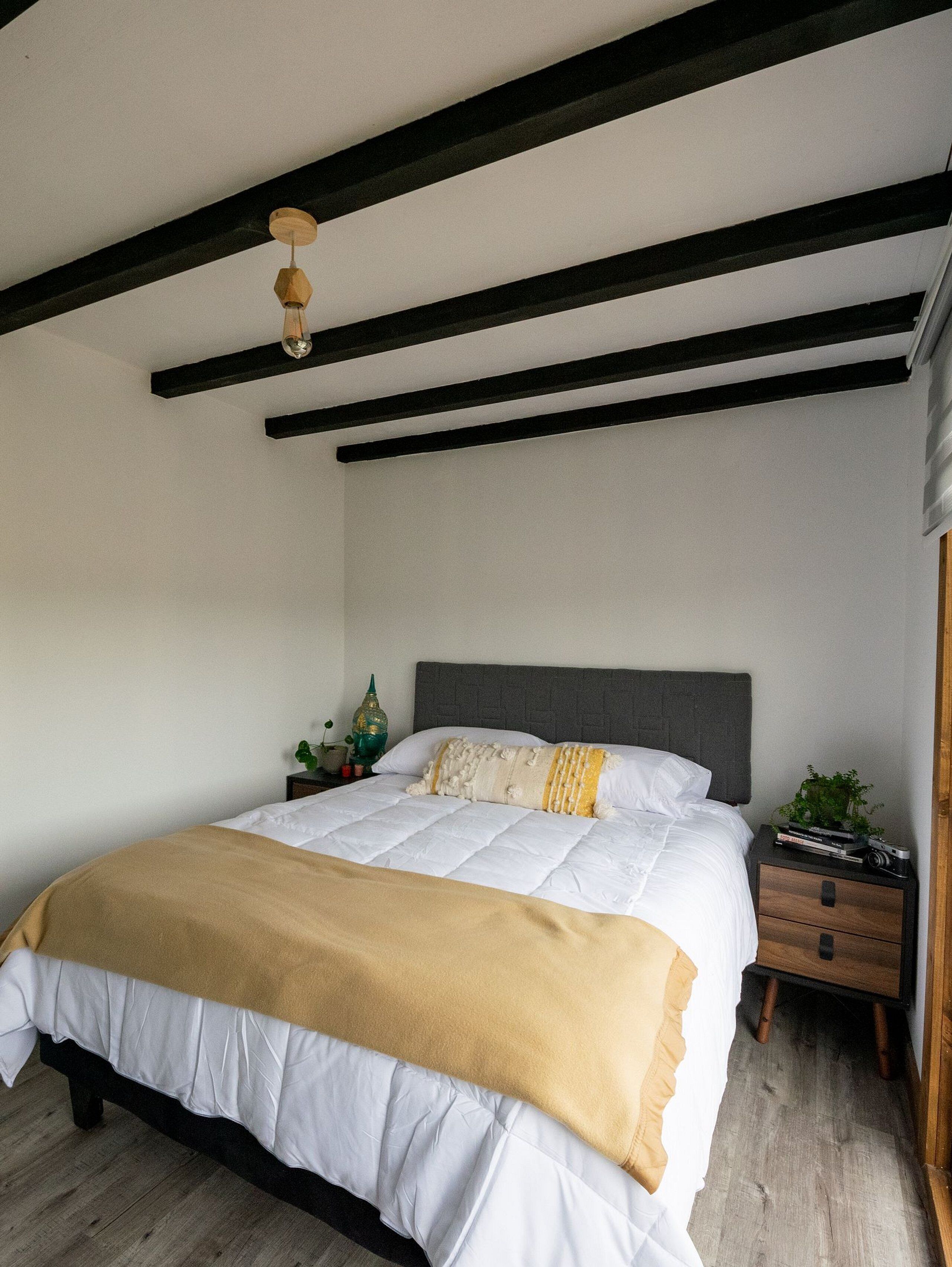 A bedroom with a bed, a nightstand, a hanging light fixture, and a wooden floor.