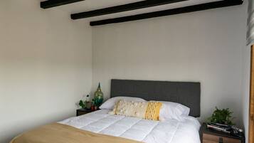 A bedroom with a bed, a nightstand, a hanging light fixture, and a wooden floor.
