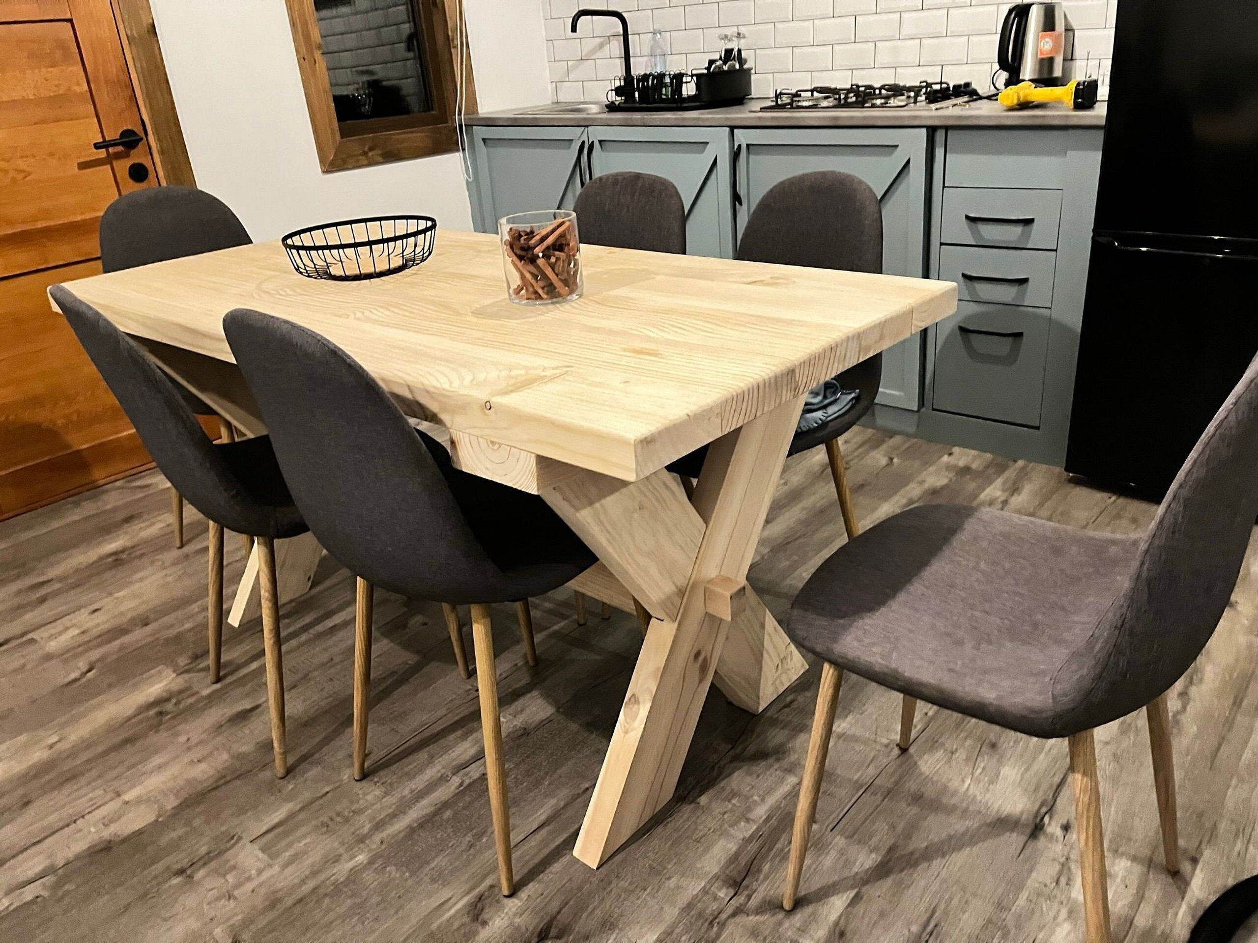Une table de salle à manger en bois, accompagnée de quatre chaises, d’un panier noir et d’un récipient en verre contenant des ustensiles.