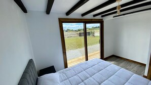 A bedroom with a large bed, wooden beams on the ceiling, and a sliding glass door leading to a balcony. - Cabañas Lawal Pto Varas (Puerto Varas)