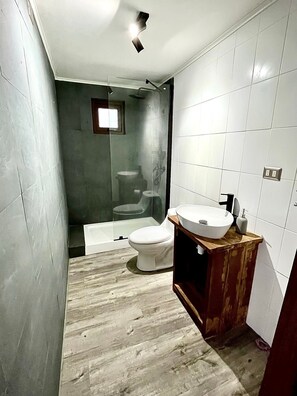 Une salle de bain moderne avec un plancher en bois, des toilettes blanches, une douche en verre et un meuble-lavabo en bois avec un évier.
