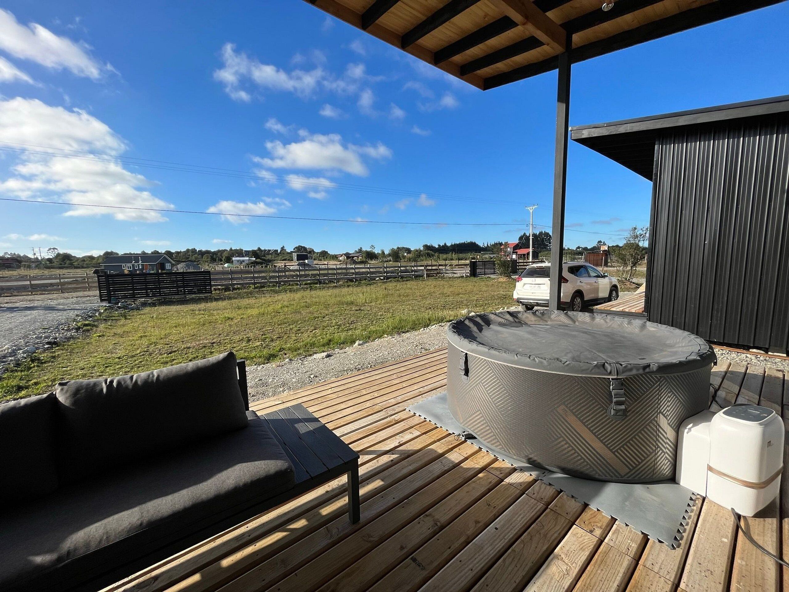 Une terrasse en bois avec un jacuzzi, un canapé et un petit bâtiment.