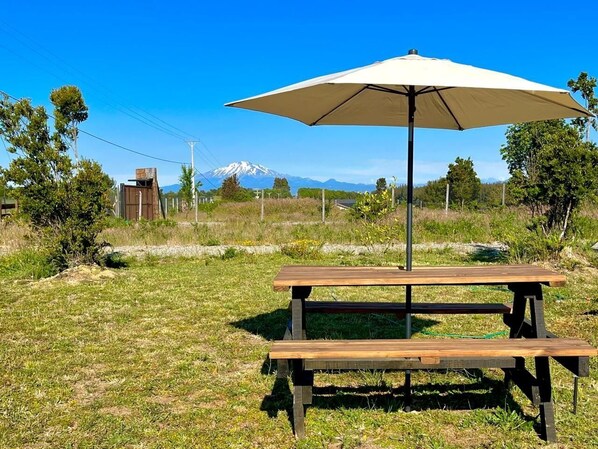 Une table de pique-nique avec un auvent, située dans un champ verdoyant, avec une montagne en arrière-plan.