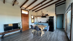 A spacious living area with a wooden dining table and chairs, a flat-screen TV, and a built-in kitchen with a refrigerator and stove. - Cabañas Lawal Pto Varas (Puerto Varas)