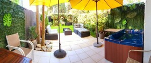 Relax in a serene outdoor space with a hot tub, comfortable seating, and lush greenery.