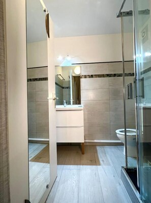 Bathroom features a glass shower enclosure, white vanity, and toilet, set against a subtle patterned backdrop.
