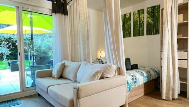 A modern bedroom with a canopy bed, a sofa, and a large window with a view of greenery.