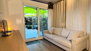 A modern living room with a sofa, a wooden table, and a sliding glass door leading to an outdoor area with a green umbrella.