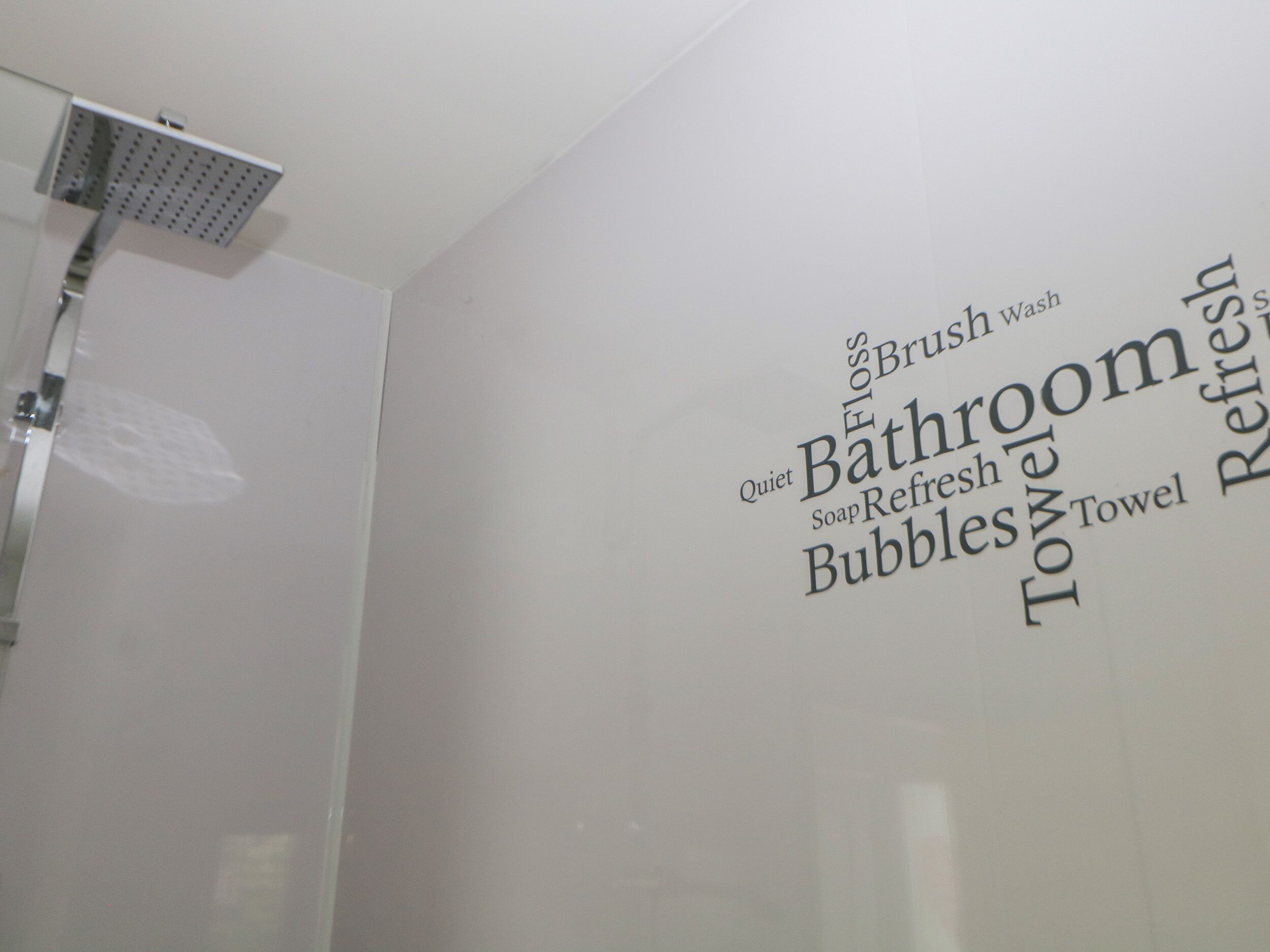 Un baño con ducha y una pared con palabras como 'Silencio', 'Baño', 'Jabón', 'Toalla' y 'Refrescado'.