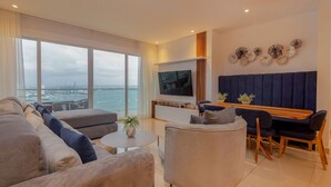 A modern living room with a large TV, comfortable seating, and a view of the city. - Condominio H2 (Cartagena)