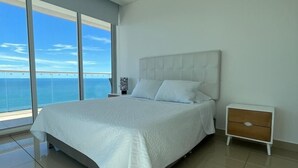 A modern bedroom with a large bed, a nightstand, and a view of the ocean. - Condominio H2 (Cartagena)