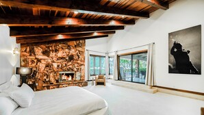 Una camera da letto con un camino in pietra, un letto, una sedia e un'ampia finestra vista verde.