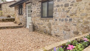 A stone building with a door and window, surrounded by gravel and flower beds. - The Stable (Narberth)