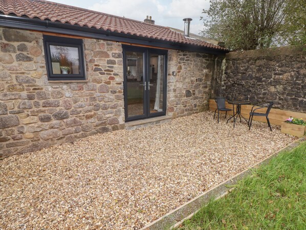 A stone building with a tiled roof, a glass door, and a patio area with chairs and a table.