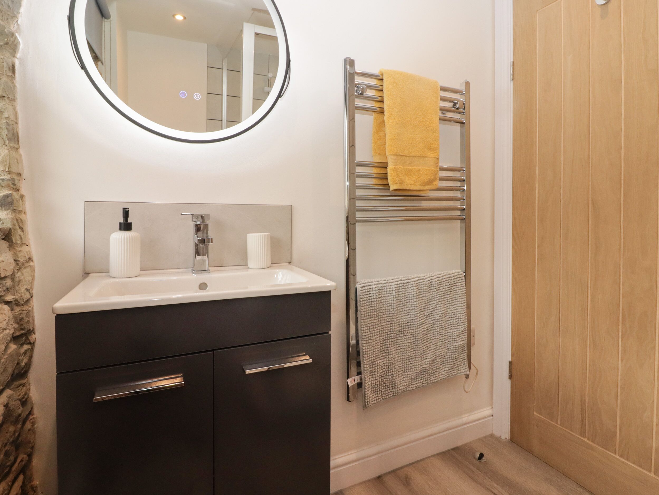 A bathroom with a sink, mirror, towel rack, and wooden door.