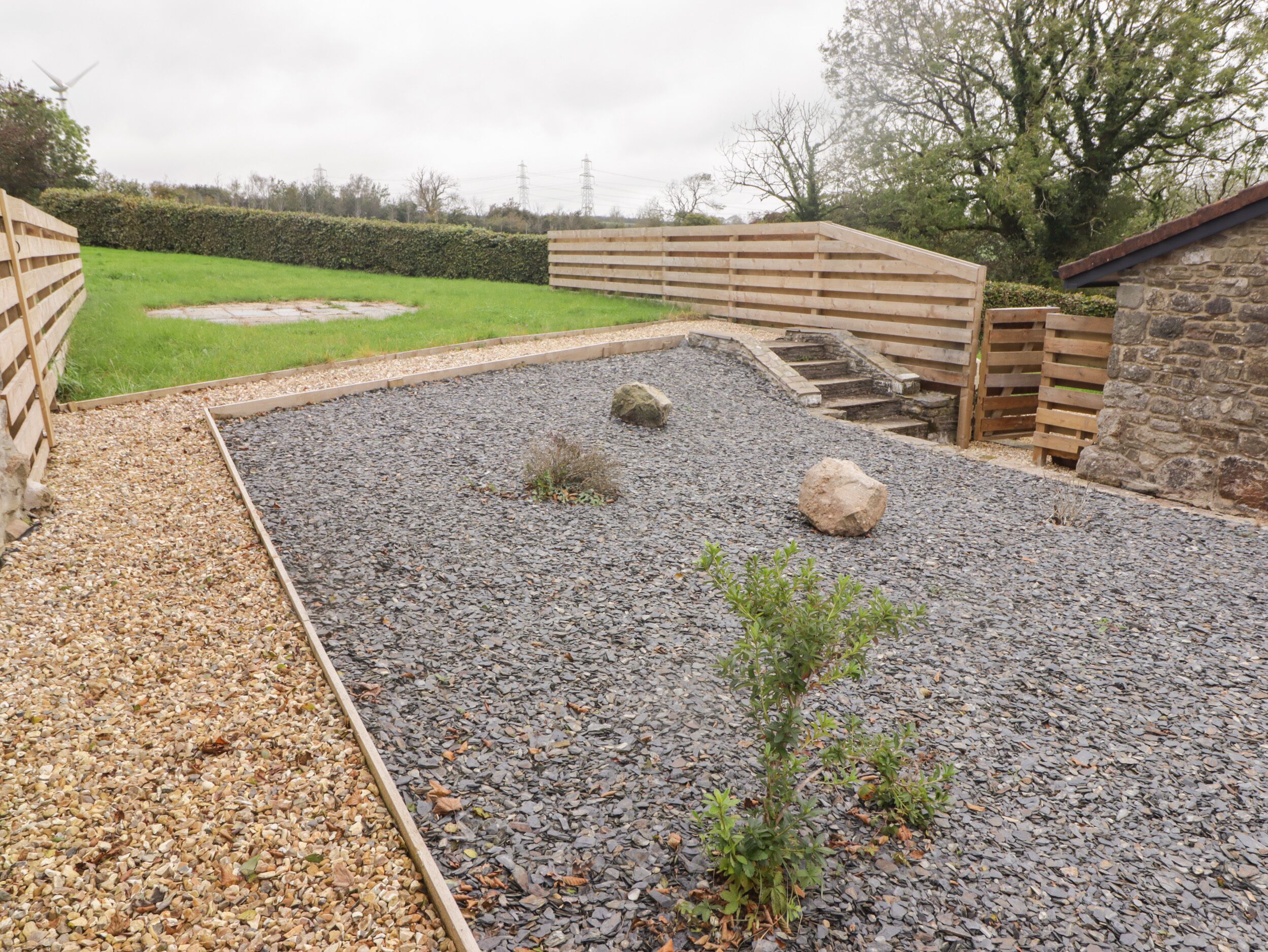 A gravel patio with wooden fences, a small plant, and a stone wall.