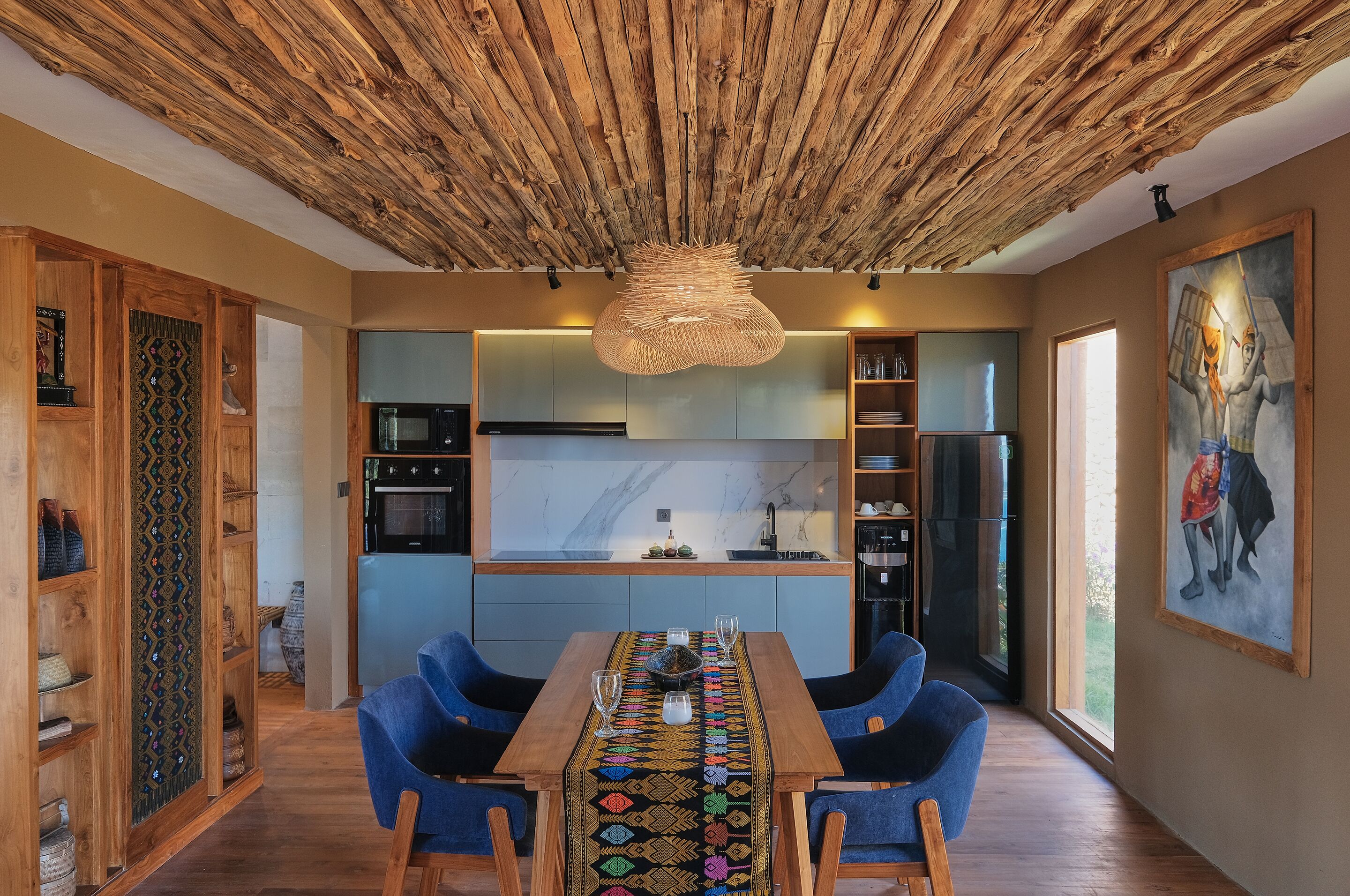 Una cocina moderna con techo de madera, una mesa de comedor con sillas azules y un amplio ventanal.
