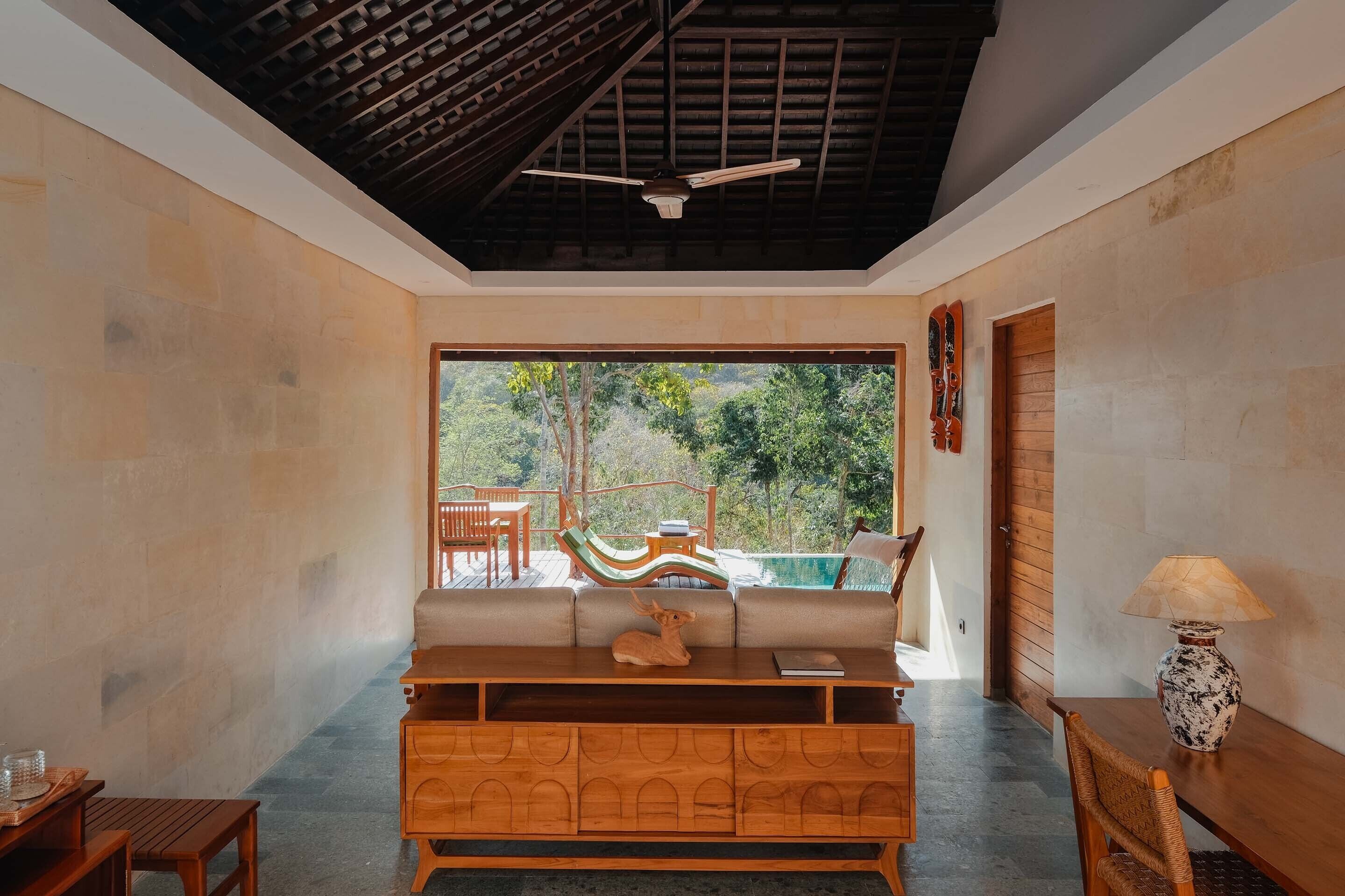 Quarto com um banco de madeira, uma mesa, uma luminária e vista para um deck externo com uma rede e piscina.