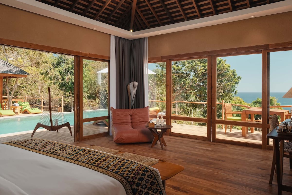 A spacious bedroom with a large bed, a view of the pool and outdoor area, and a wooden ceiling.