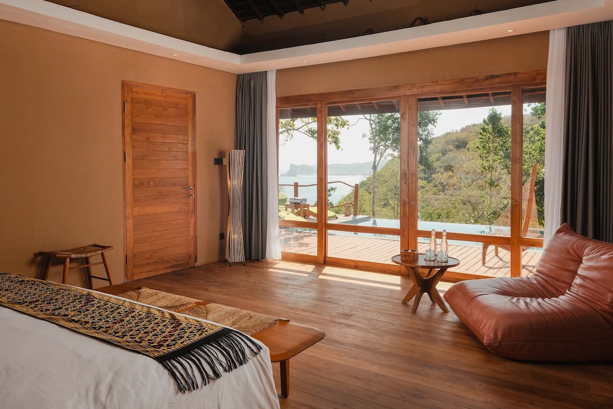 A spacious room with a large bed, a leather sofa, a small table, and a view of a deck and natural landscape.