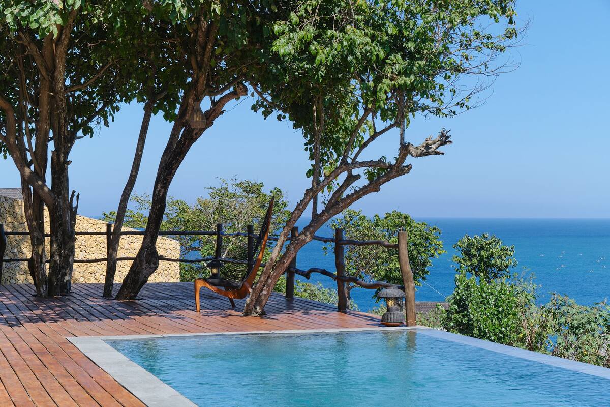 A wooden deck with a pool, overlooking the sea.