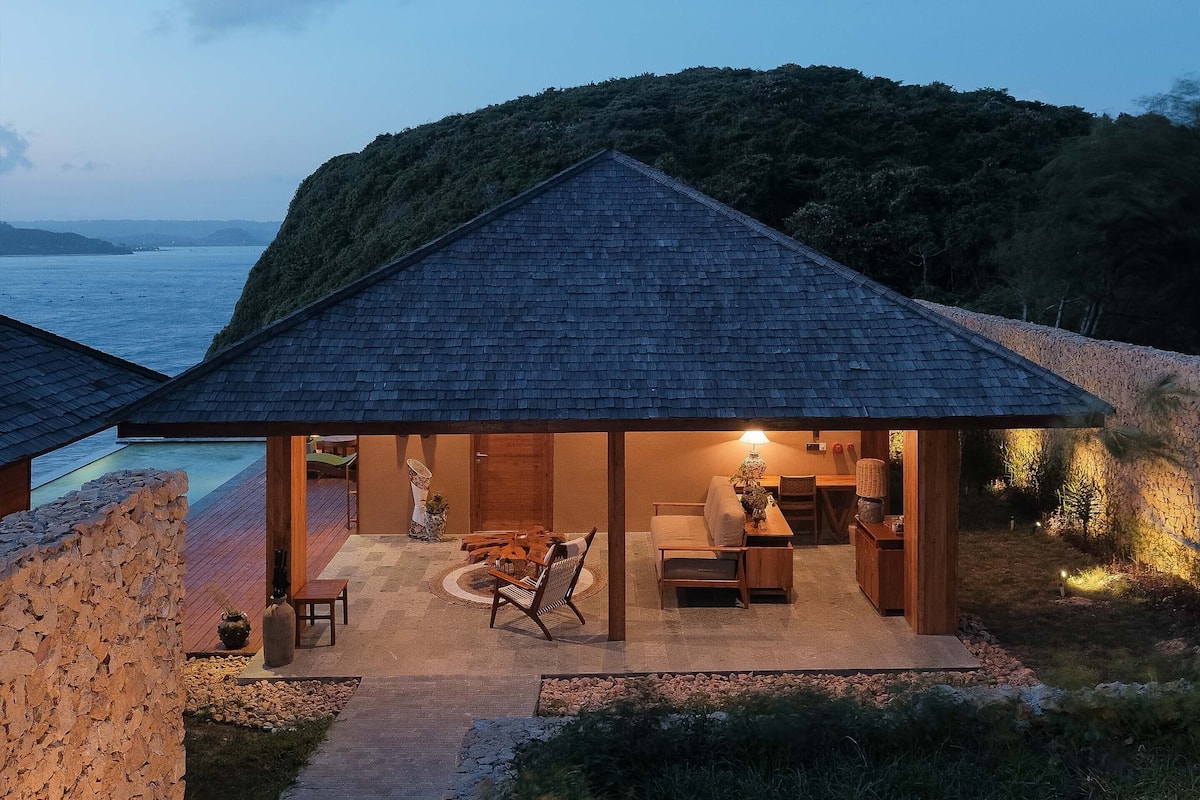 A modern house with a covered patio overlooking a pool and the sea.
