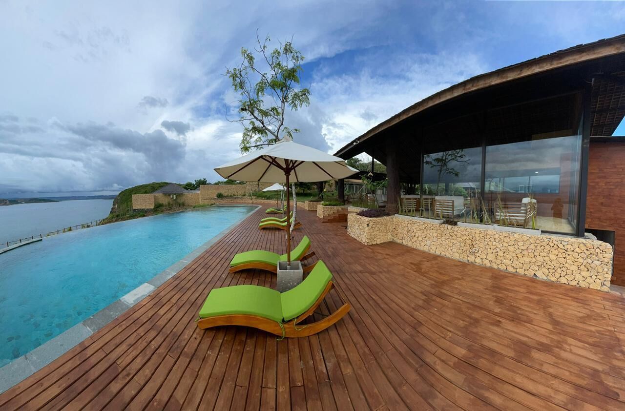 A wooden deck with green lounge chairs and a pool.