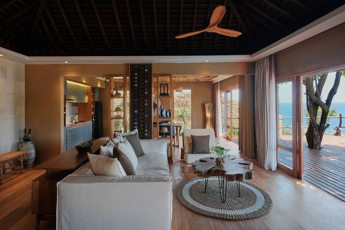 A spacious living area with a wooden ceiling, a large sofa, a coffee table, and a view of the ocean.