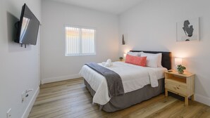 Un dormitorio con cama, mesita de noche, lámpara y una obra de arte en la pared.