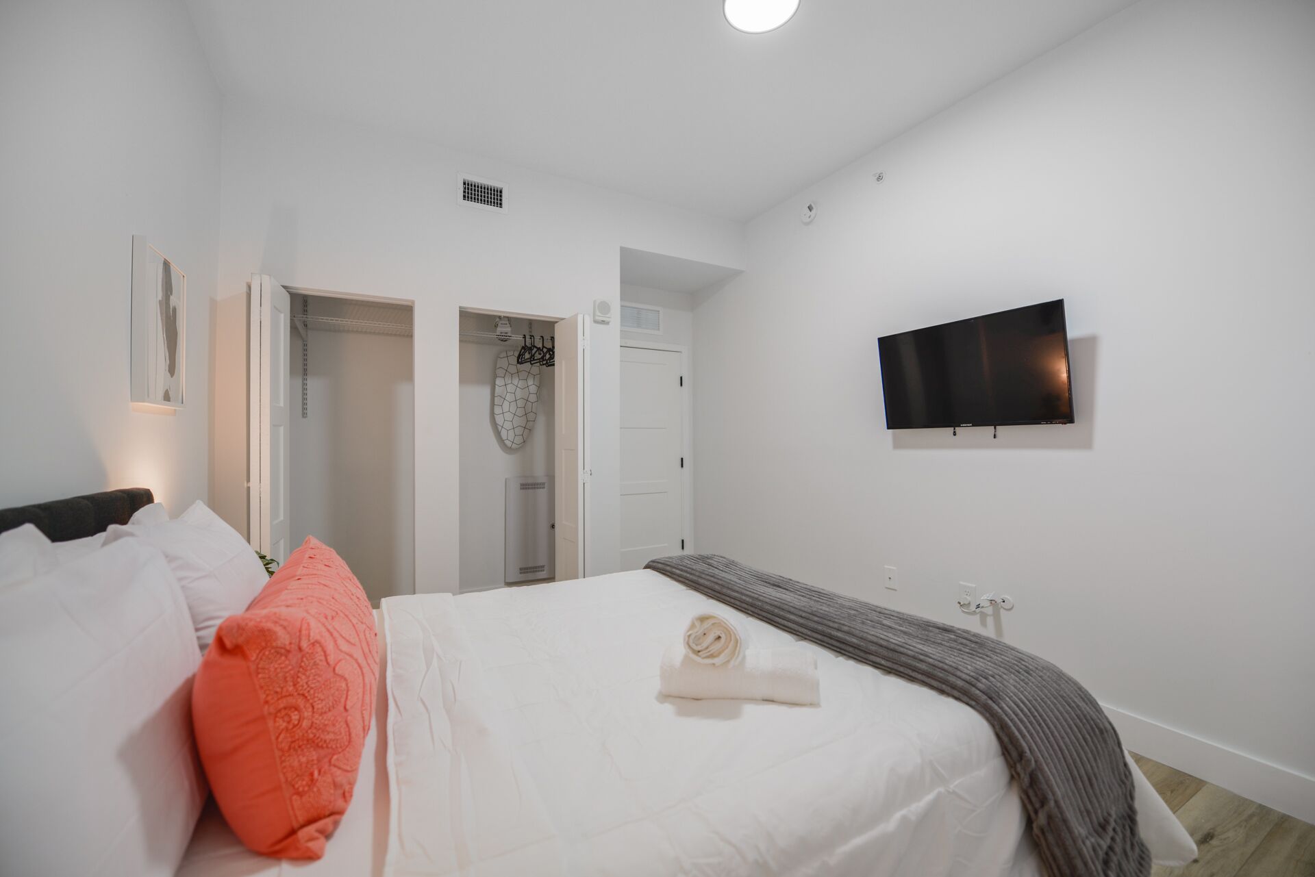 Ein Schlafzimmer mit Bett, Wandfernseher und Schrank mit Spiegel.