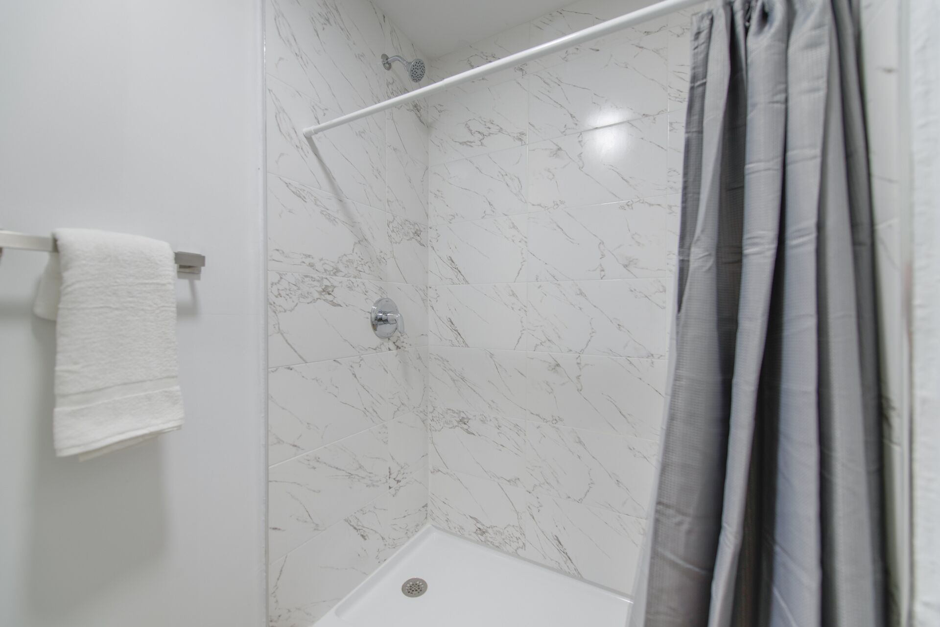 Une salle de bain moderne avec un espace douche, des murs en marbre blanc et un porte-serviettes.