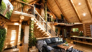 A log cabin interior with a staircase, a living room, a dining area, and a sign that reads 'Jungle'.