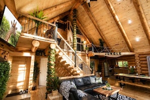 A log cabin interior with a staircase, a living room, a dining area, and a sign that reads 'Jungle'. - Welcome to the Jungle | Log cabine | Spa (Saint-Philémon)