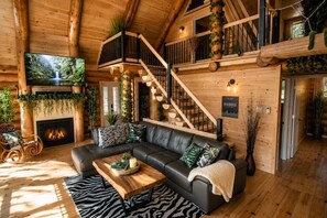 A log cabin interior with a fireplace, a black leather sofa, a wooden coffee table, a zebra-patterned rug, and a staircase. - Welcome to the Jungle | Log cabine | Spa (Saint-Philémon)