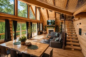 A spacious wooden cabin with a large dining table, a sofa, and a staircase. - Welcome to the Jungle | Log cabine | Spa (Saint-Philémon)
