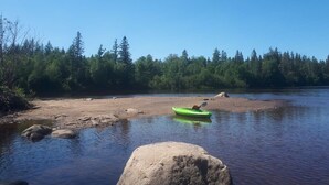 Un kayakiste sur une rivière paisible, bordée d’une forêt.