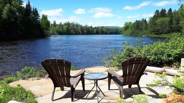Deux fauteuils Adirondack sont placés face à un lac, dont les rives sont bordées d’une forêt.