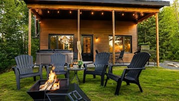 A wooden cabin with a covered patio, outdoor seating, and a fire pit.