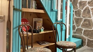 A cozy reading nook with teal walls, a wooden bookshelf, two chairs, and a stone wall.