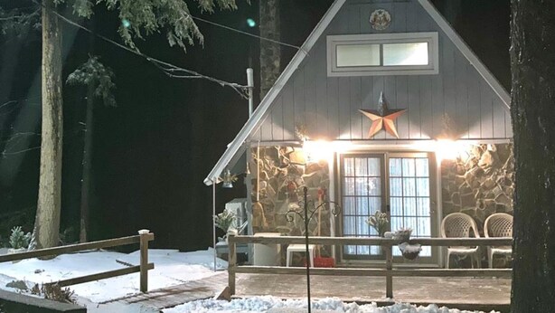A cabin with a stone exterior, a star decoration above the entrance, and a porch with benches.