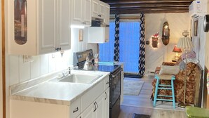 A kitchen with white cabinets, a stove, and a sink. There is a patterned rug on the floor and a blue stool.