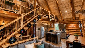 A log cabin interior with a wooden staircase, a kitchen, a dining area, and a cozy living room with a sofa. - Private Heated Pool | Spa | Party | The Animal (Saint-Philémon)