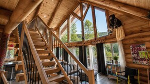 A wooden cabin interior with a spiral staircase, large windows, and a rustic decor. - Private Heated Pool | Spa | Party | The Animal (Saint-Philémon)