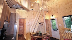 A wooden cabin interior with a kitchen, dining area, and a staircase leading to a loft. - Waterfront Cabin with Spa | Le Colvert (Shannon)
