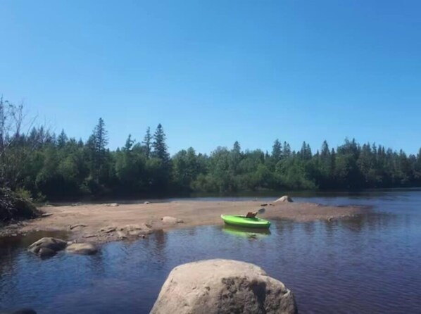 Une rivière paisible, avec un kayak vert sur la rive et un grand rocher au premier plan.