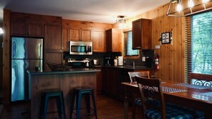 Une cuisine dotée de meubles en bois, d’un four à micro-ondes, d’un réfrigérateur, d’un évier et d’un coin repas avec une table et des chaises.