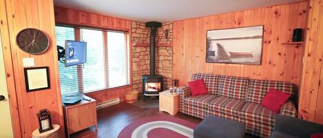 Un interior de cabaña acogedor, con pared de piedra, paredes de madera, un sofá a cuadros, un televisor y una chimenea.